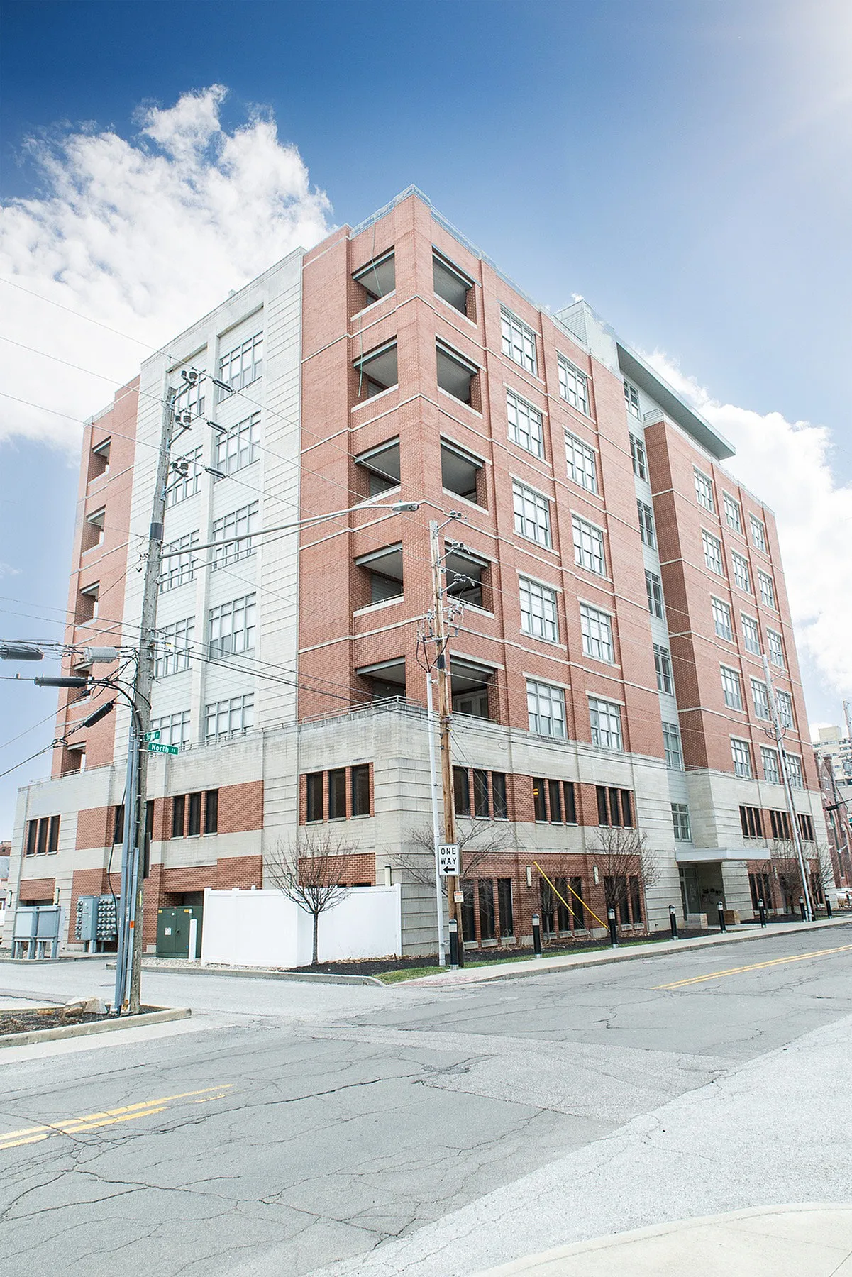 Modern urban apartment building with striking red brick facade and spacious balconies against a bright blue sky.