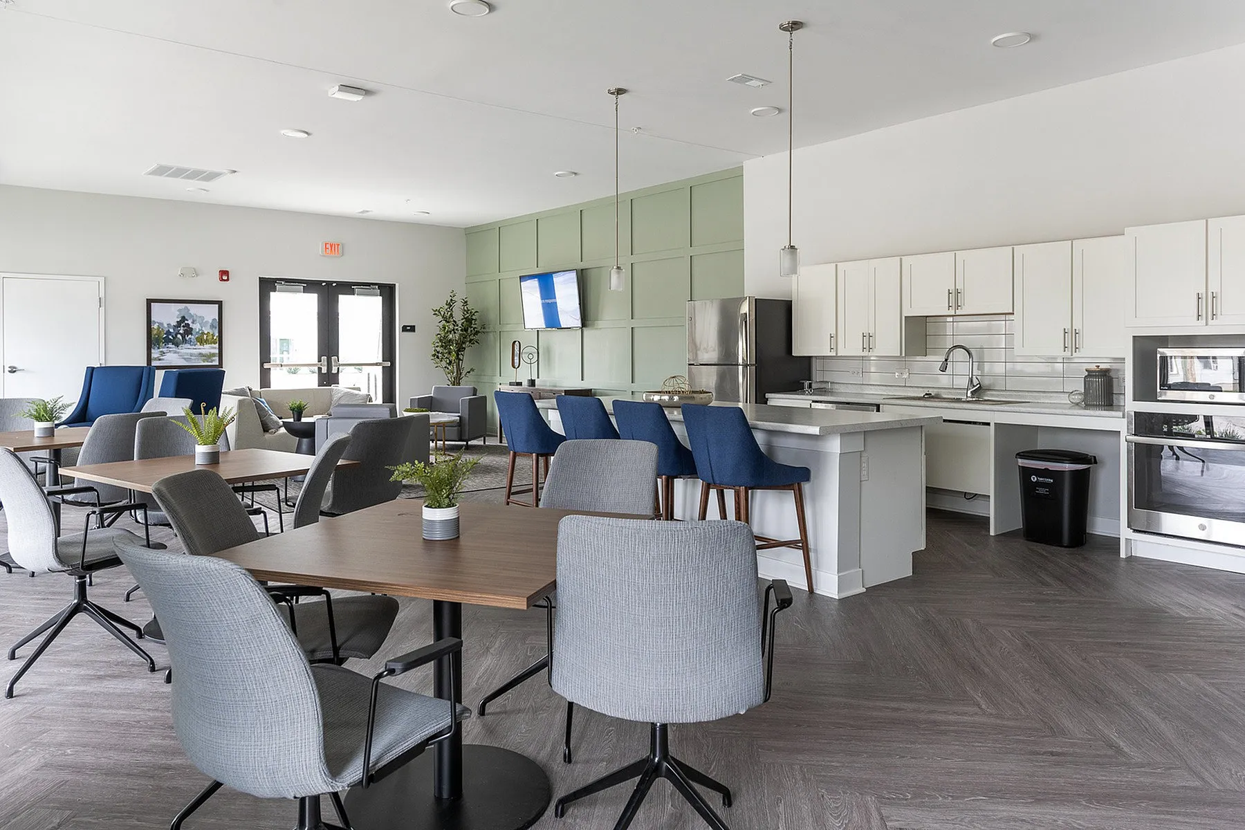 Elegant community space featuring a modern kitchen with sleek white cabinets, stylish dining tables, and comfortable seating with vibrant blue chairs, perfect for social gatherings.