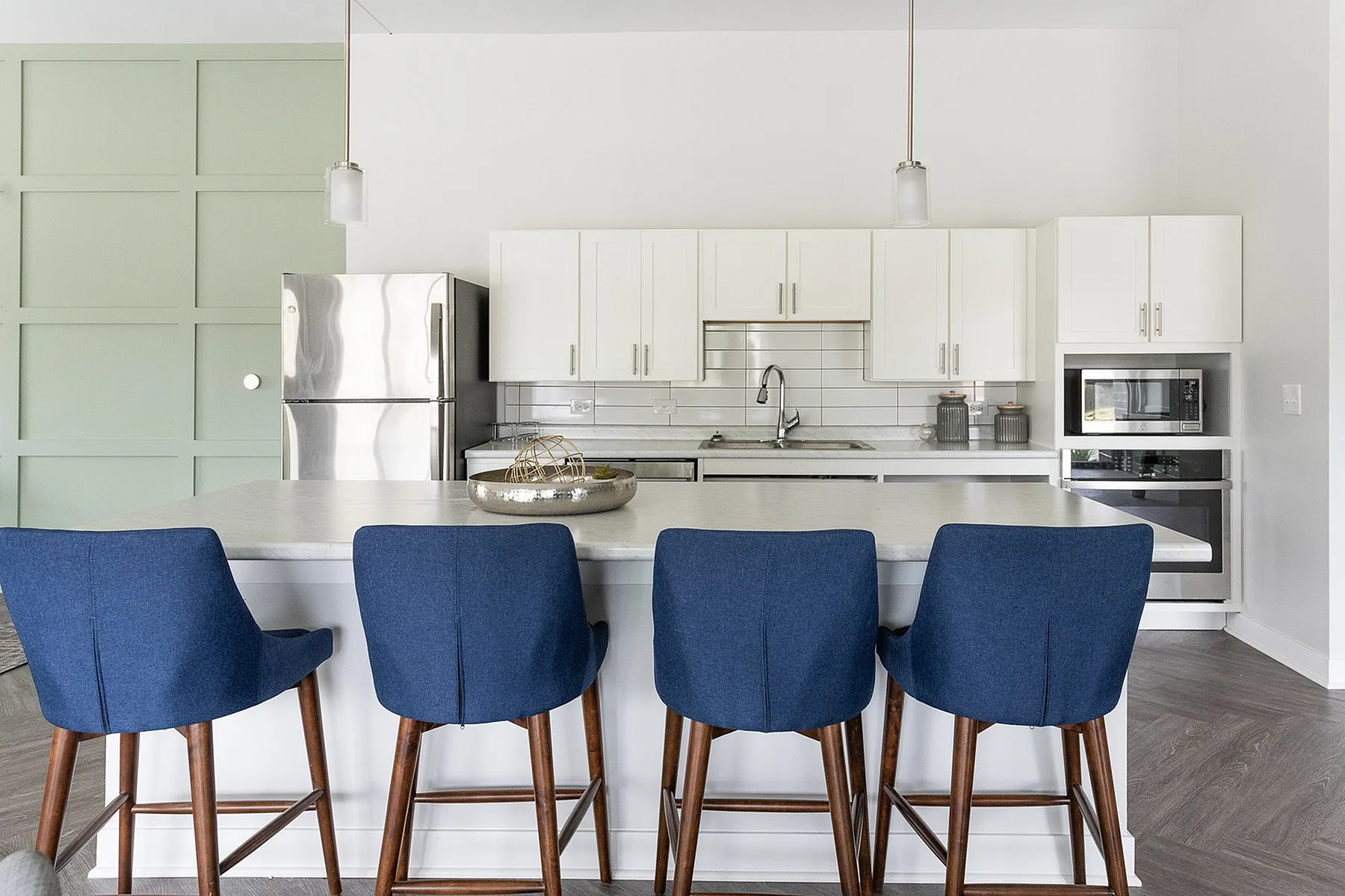 Modern kitchen featuring sleek white cabinetry, stainless steel appliances, and an elegant breakfast bar with plush blue chairs.