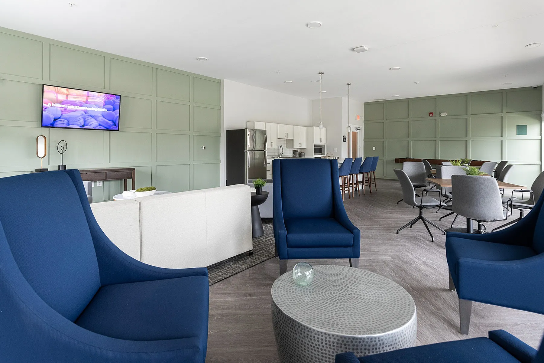 Modern open-concept lounge with elegant blue seating, chic dining area, and a sleek kitchen in a bright, welcoming space.
