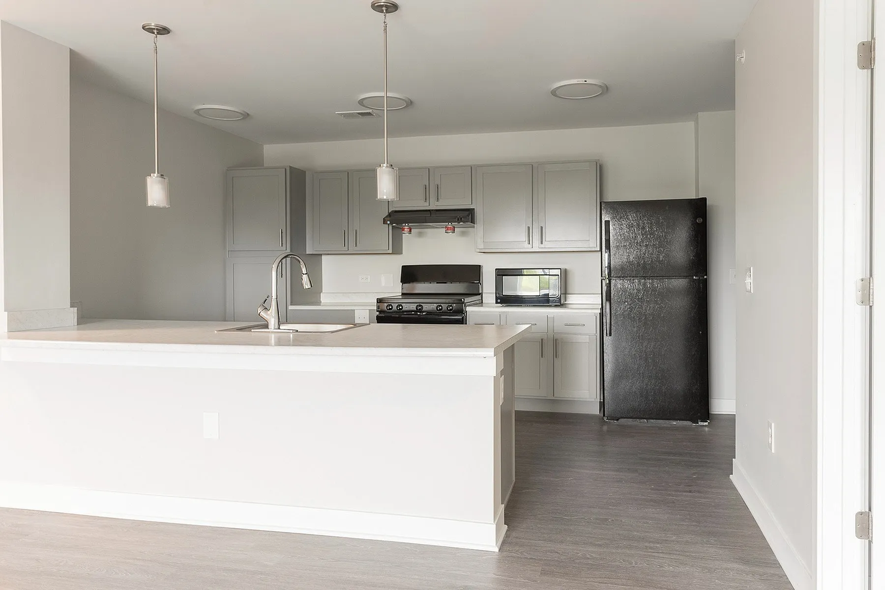Modern kitchen with sleek gray cabinets, black appliances, and a spacious white marble island, enhanced by elegant pendant lighting.