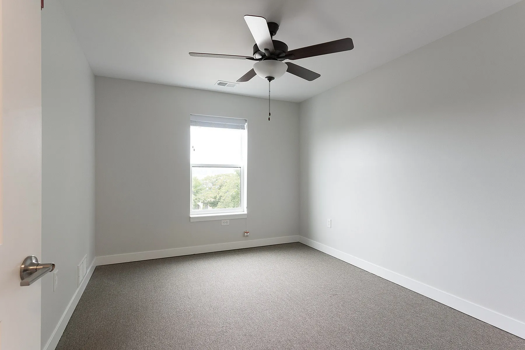 Bright bedroom with fresh paint, modern ceiling fan, and a sunny window offering a serene outdoor view.