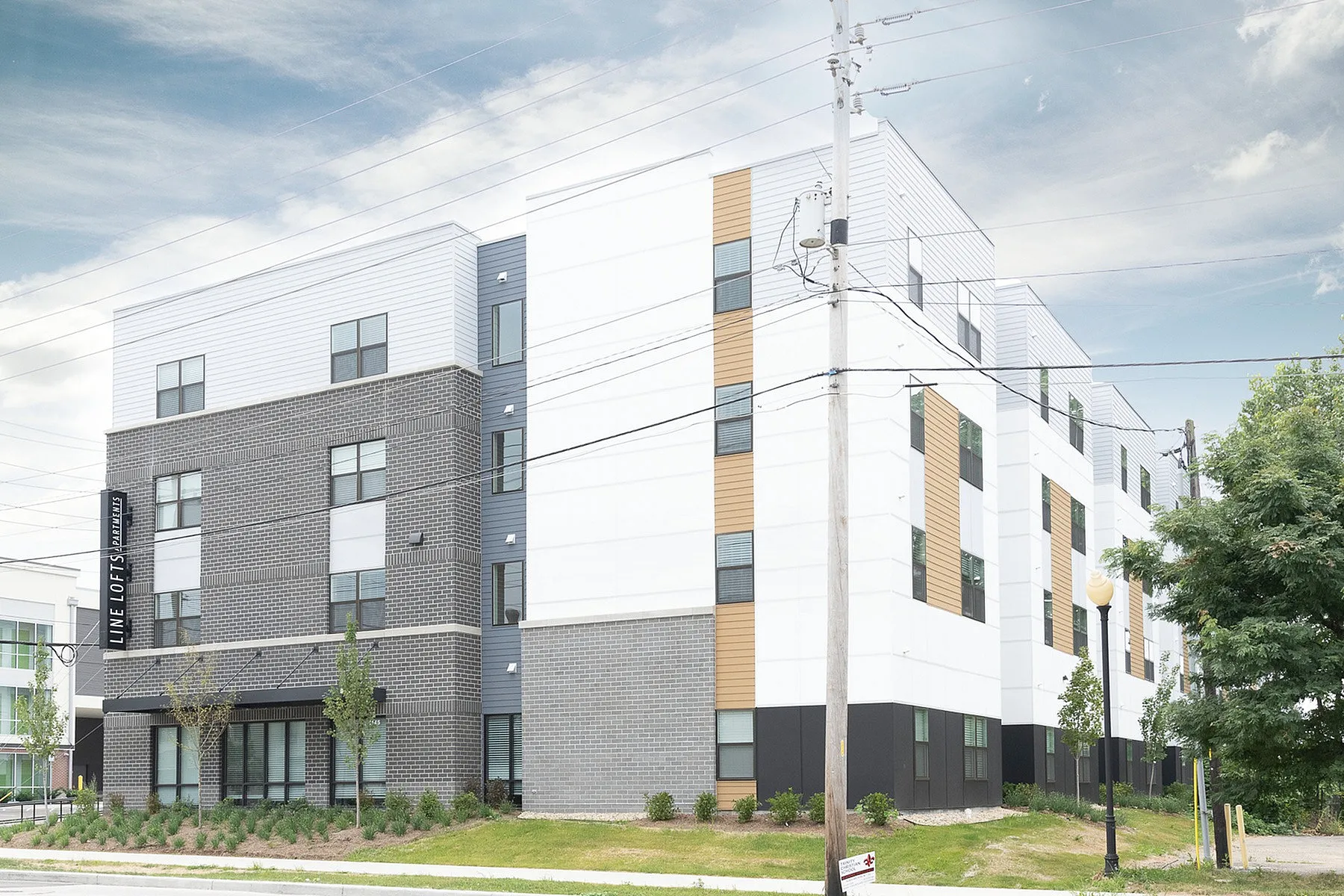 Modern apartment complex with a stylish facade, featuring a blend of brick and contemporary paneling, surrounded by fresh landscaping.