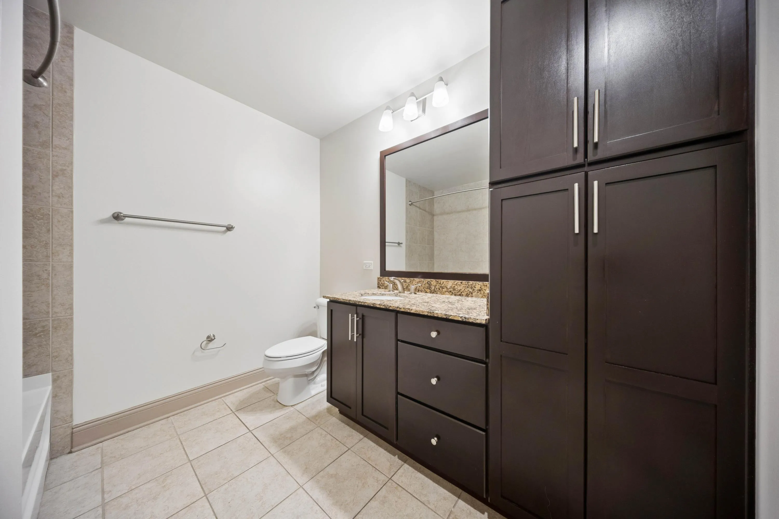 Elegant bathroom featuring dark wood cabinetry, granite countertop, and modern amenities with a spacious layout.
