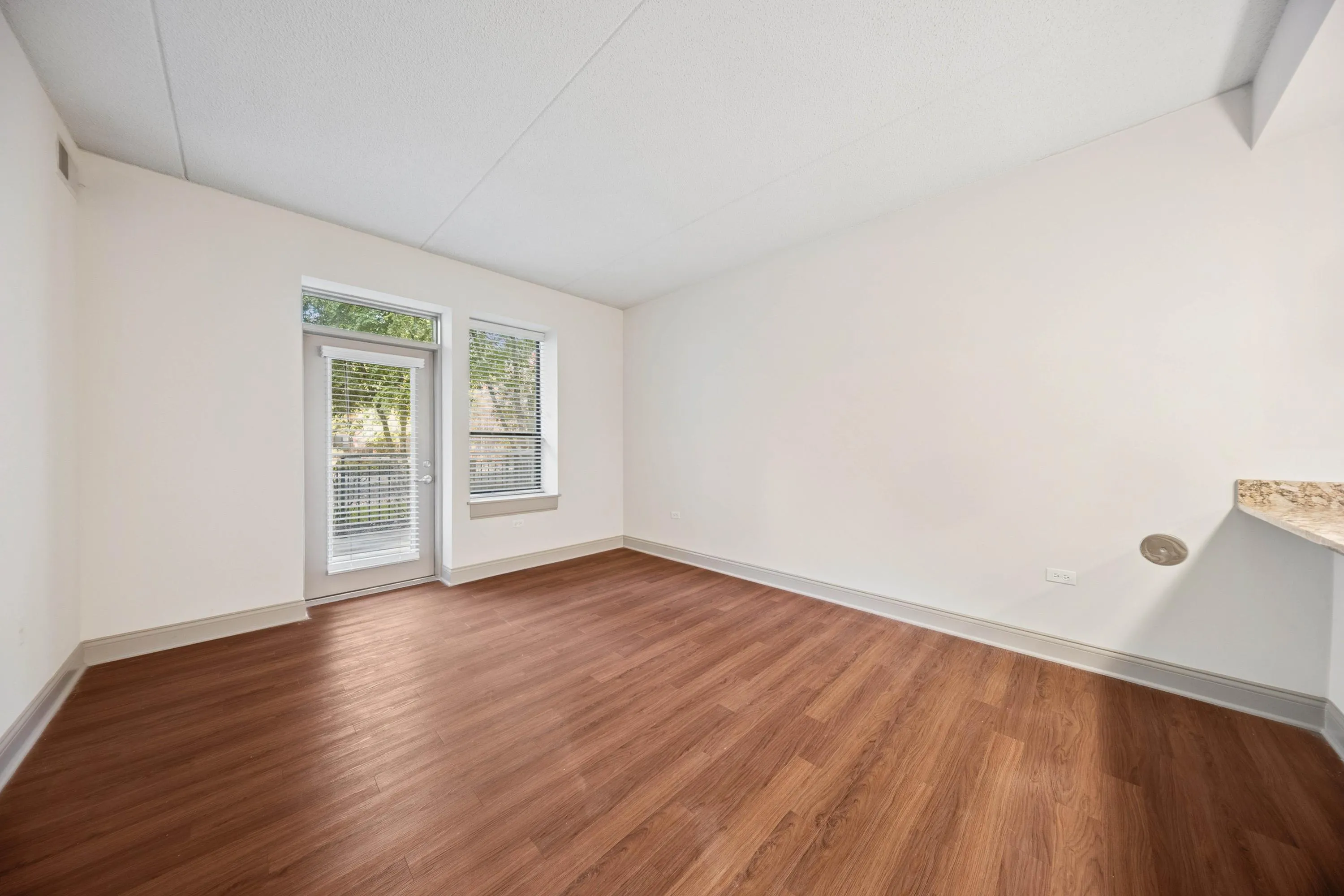 Bright, modern room with sleek hardwood floors, large windows, and glass door opening to a serene view, perfect for a cozy home setting.