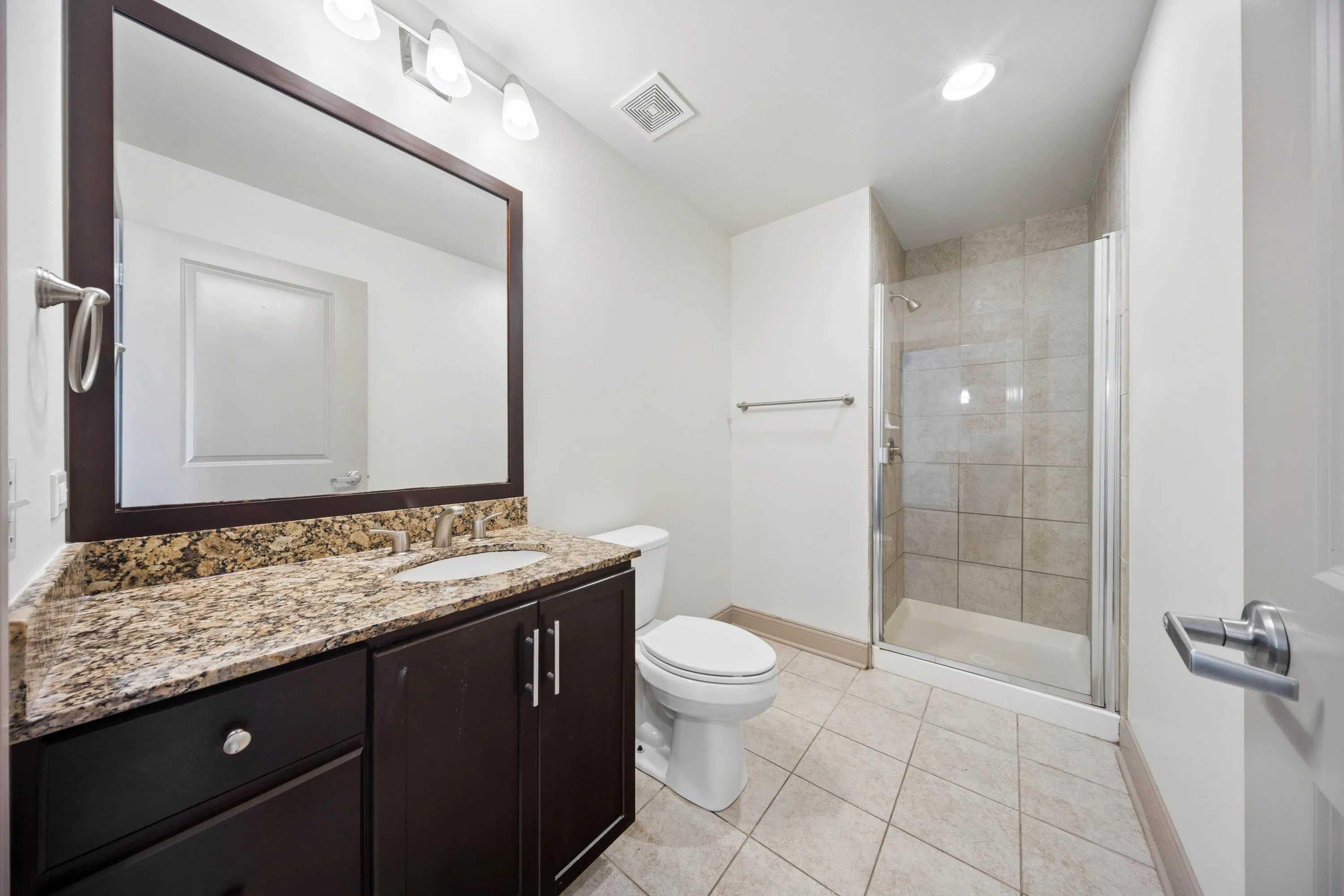 Elegant bathroom featuring a granite countertop, dark wood vanity, and a spacious tiled shower.