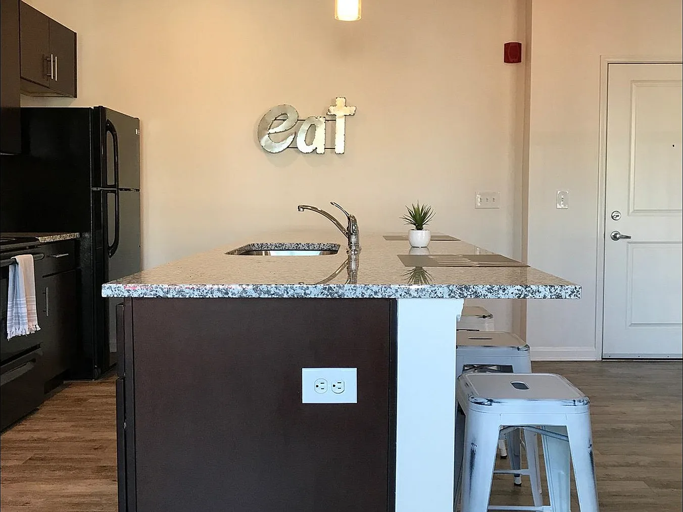 Chic modern kitchen with sleek dark wood island, elegant lighting, and stylish bar stools, offering a welcoming space for culinary creativity.