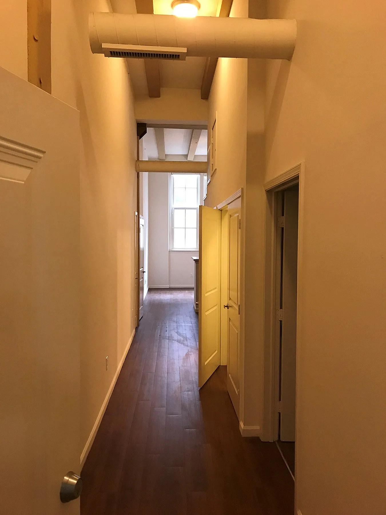 Inviting hallway with elegant wood flooring leading to a bright and spacious room, showcasing modern design and high ceilings.