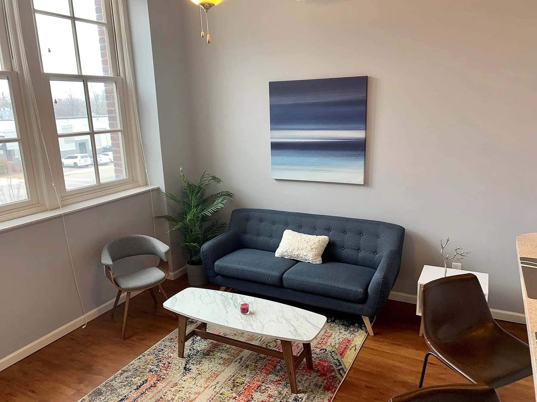 Charming living room with large windows, modern navy sofa, elegant marble coffee table, and vibrant artwork.