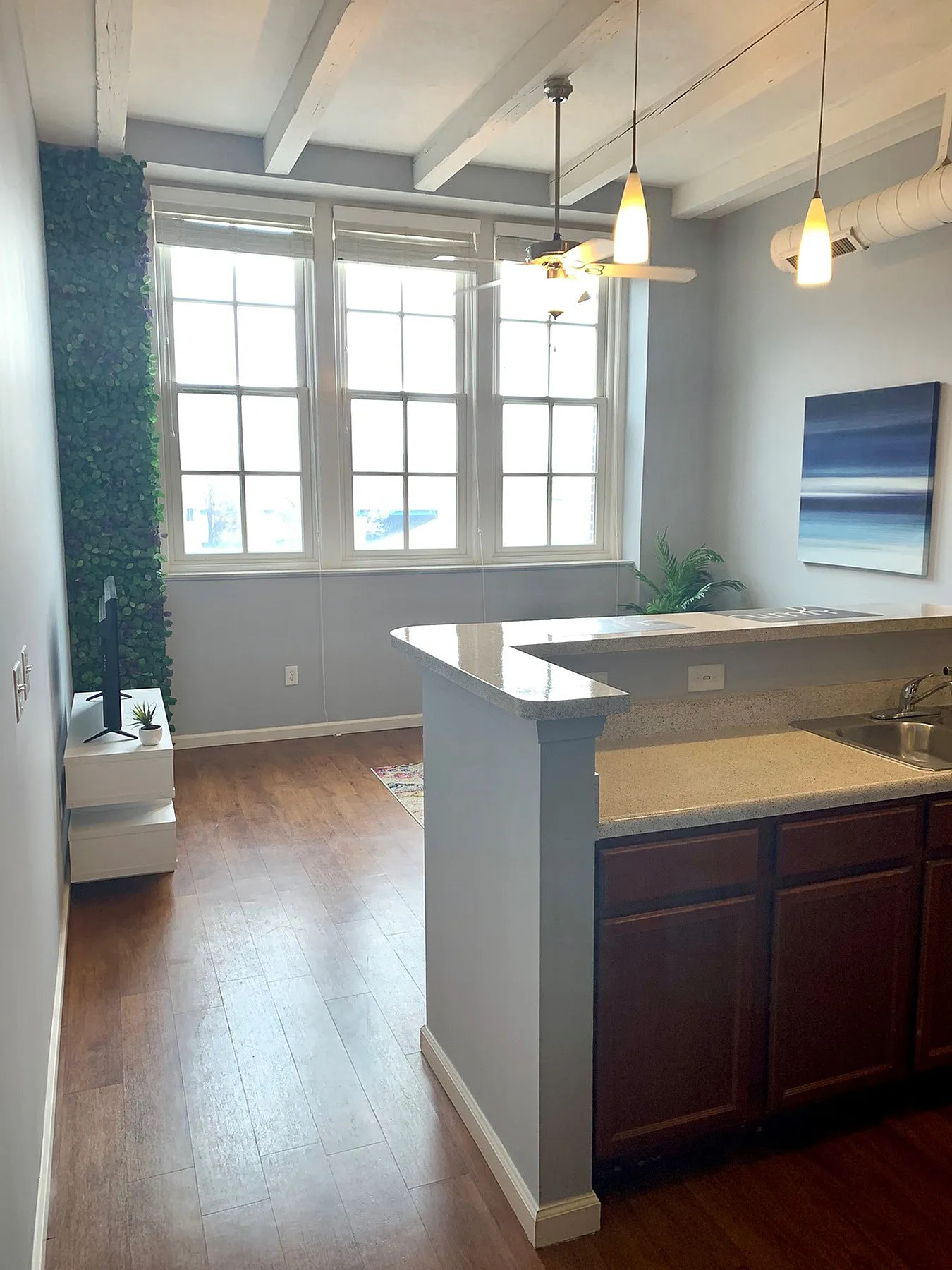 Bright apartment kitchen with sleek countertops, pendant lighting, and large windows overlooking a modern living area.