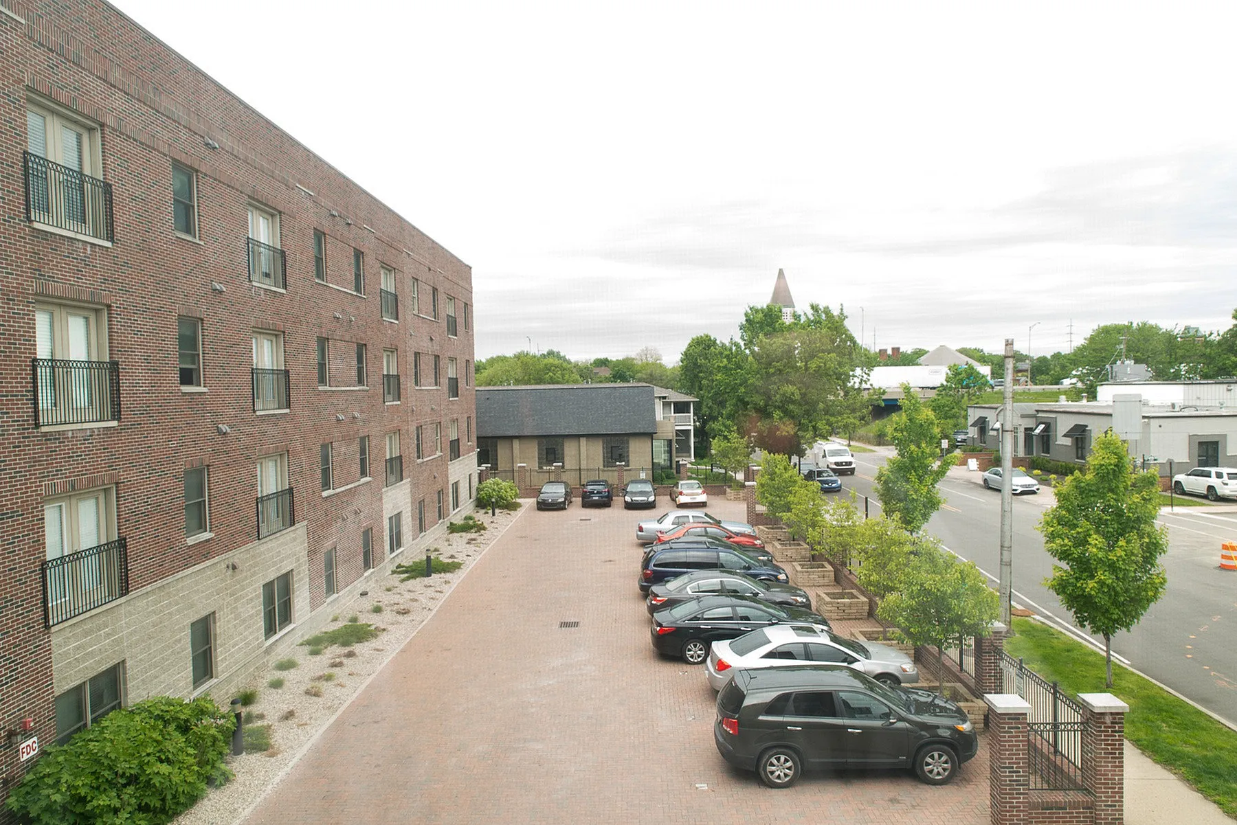 Charming brick apartment building with ample parking space, set in a lush, tree-lined suburban neighborhood.