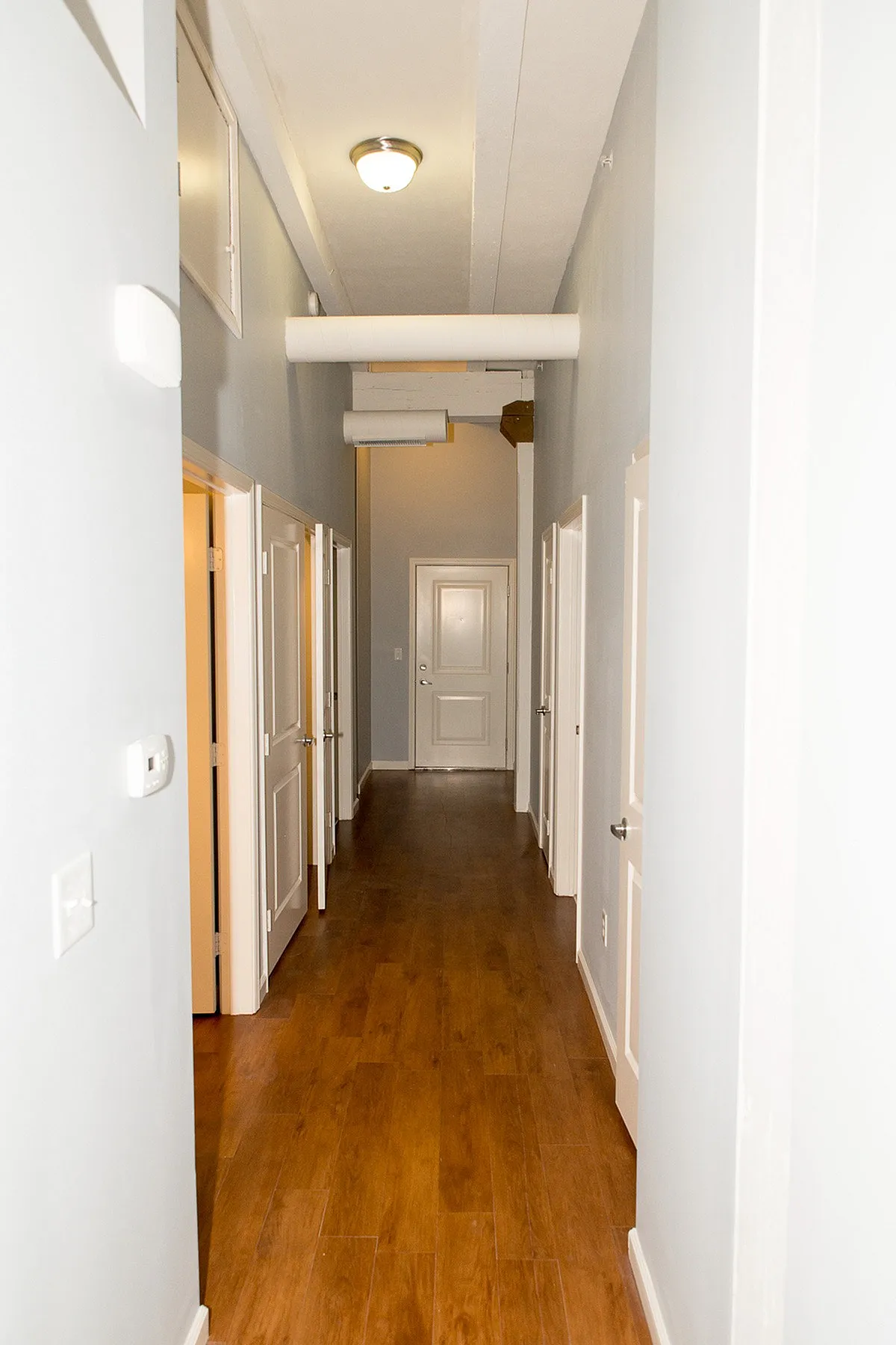 Inviting hallway with elegant wooden floors and multiple doorways leading to spacious rooms, perfect for modern living.