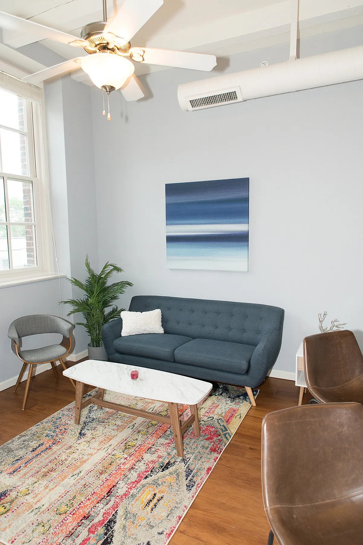 Chic apartment living room with a modern blue sofa, elegant decor, and a vibrant abstract rug under a stylish ceiling fan.