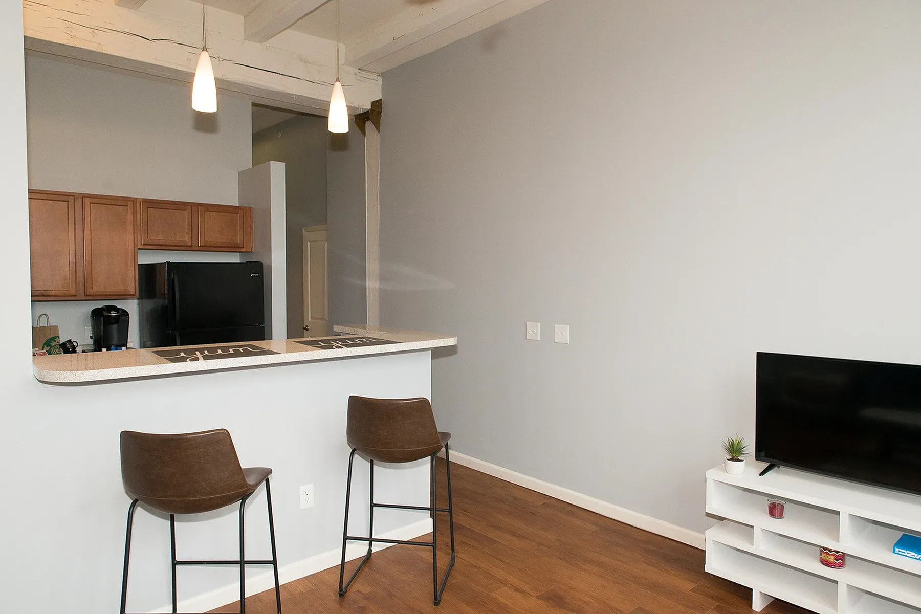 Modern apartment interior showcasing a sleek kitchen with wooden cabinets, inviting breakfast bar with stools, elegant lighting, and cozy living area with a stylish TV setup.
