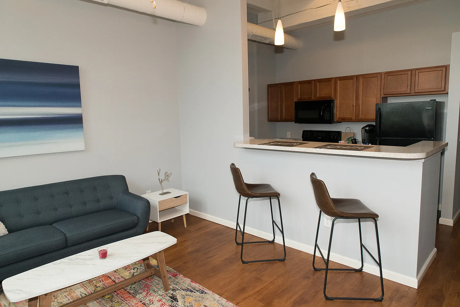 Chic apartment living space showcasing a modern open-concept layout with a cozy sofa, stylish breakfast bar, and contemporary kitchen, enhanced by warm wood flooring and elegant lighting.