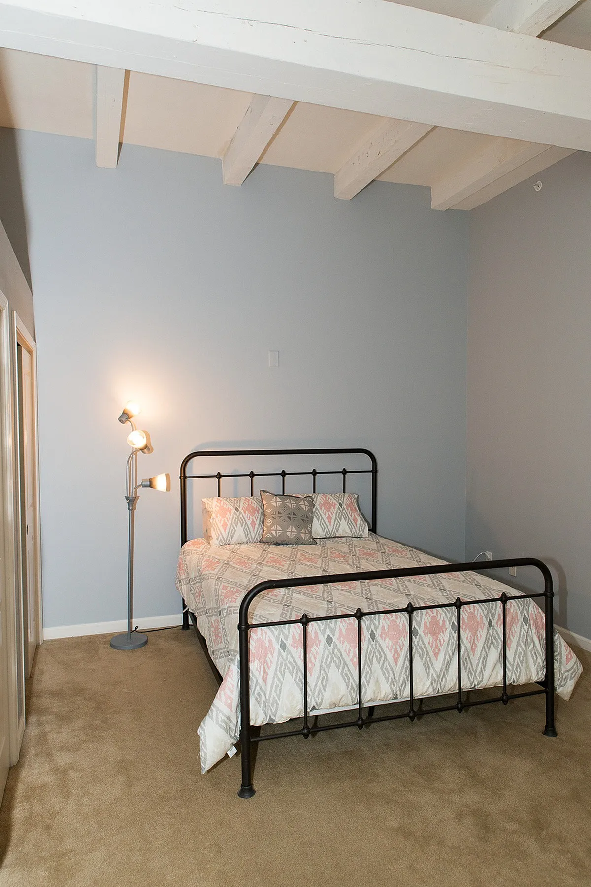 Cozy bedroom featuring a stylish metal-framed bed with patterned bedding, accented by a modern floor lamp and neutral carpet.