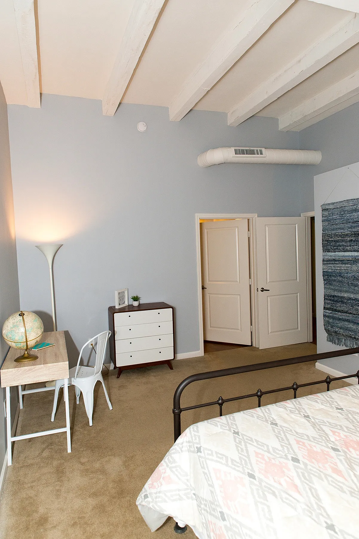Bright and airy bedroom with wooden beams, stylish desk, and cozy atmosphere.