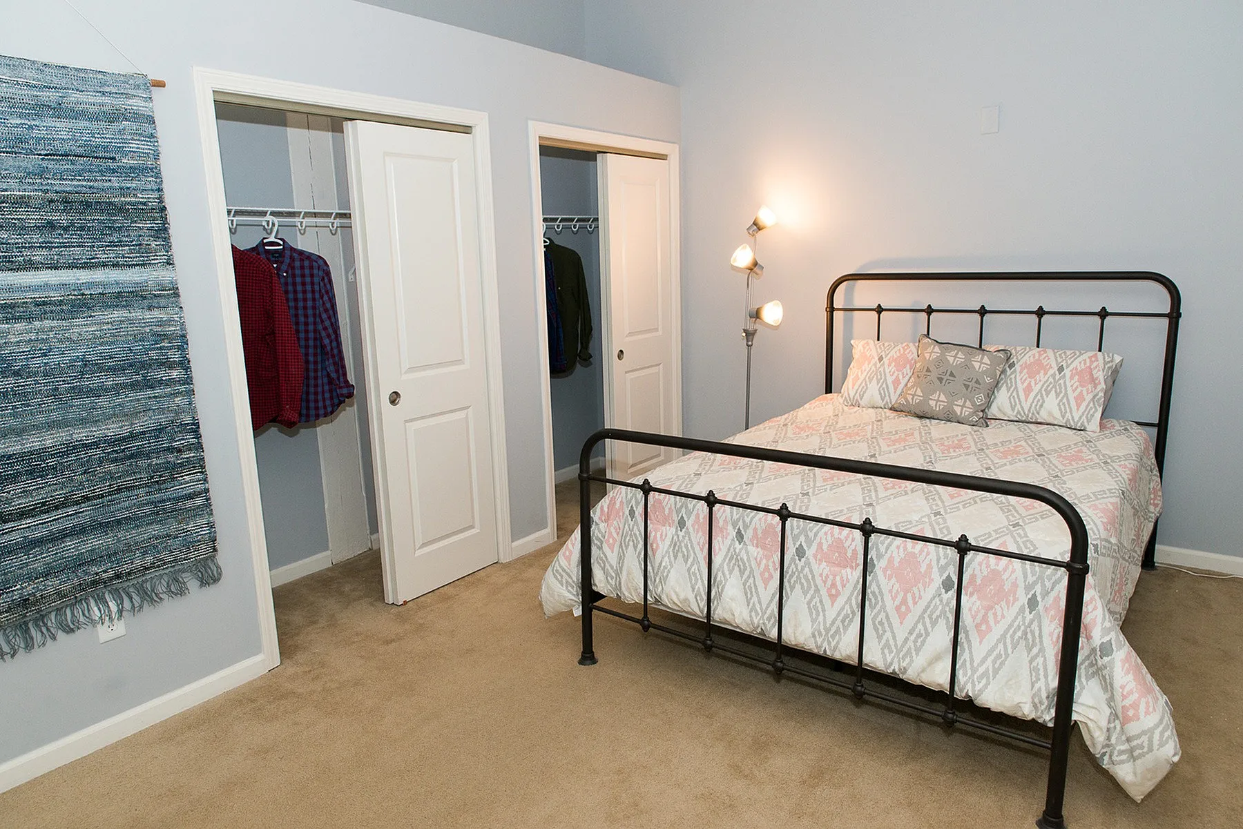 Cozy bedroom featuring a stylish metal bed frame, patterned bedding, and double closets, bathed in warm light.