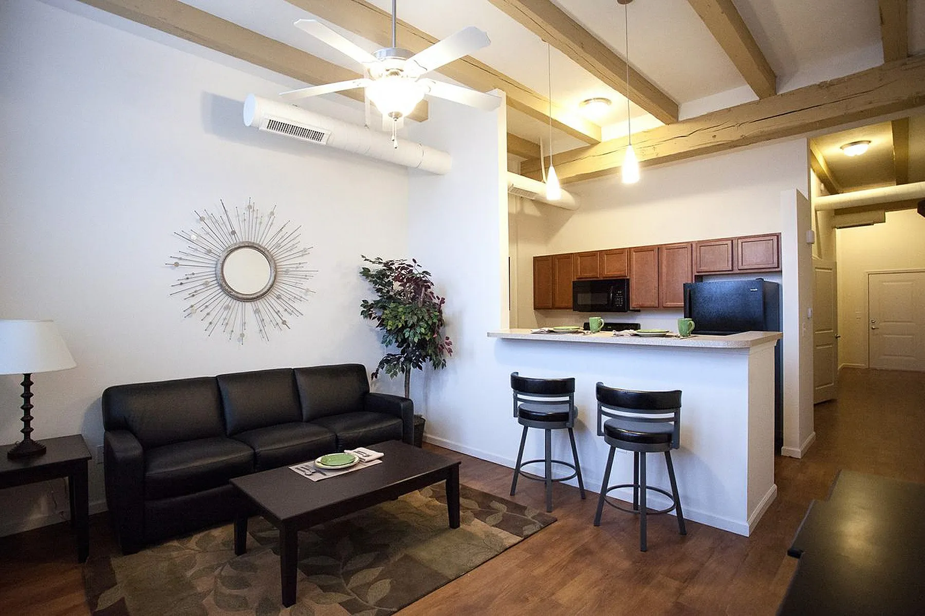 Inviting open-plan living room and kitchen with stylish black furnishings, modern decor, and wooden beams for a cozy atmosphere.