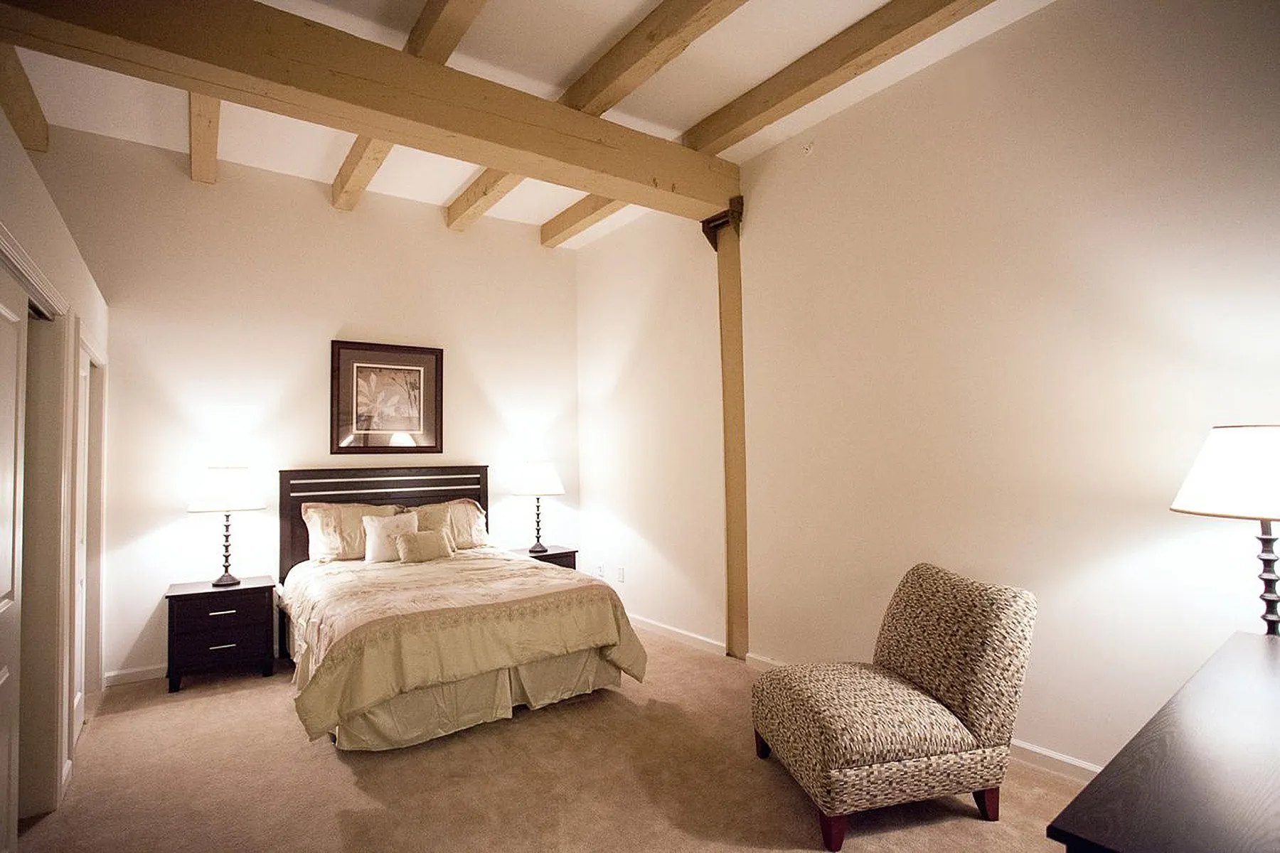 Elegant bedroom with exposed wooden beams, featuring a cozy bed, stylish nightstands, and soothing warm lighting.