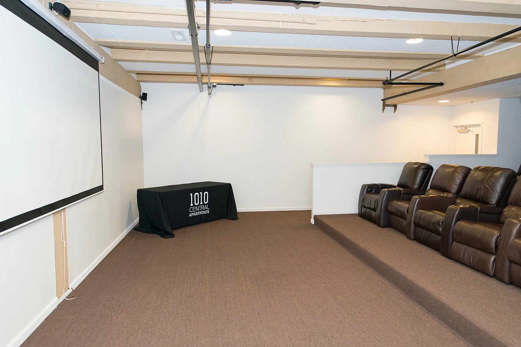 Cozy apartment theater room with tiered leather seating and a large projection screen at 1010 Central Apartments.
