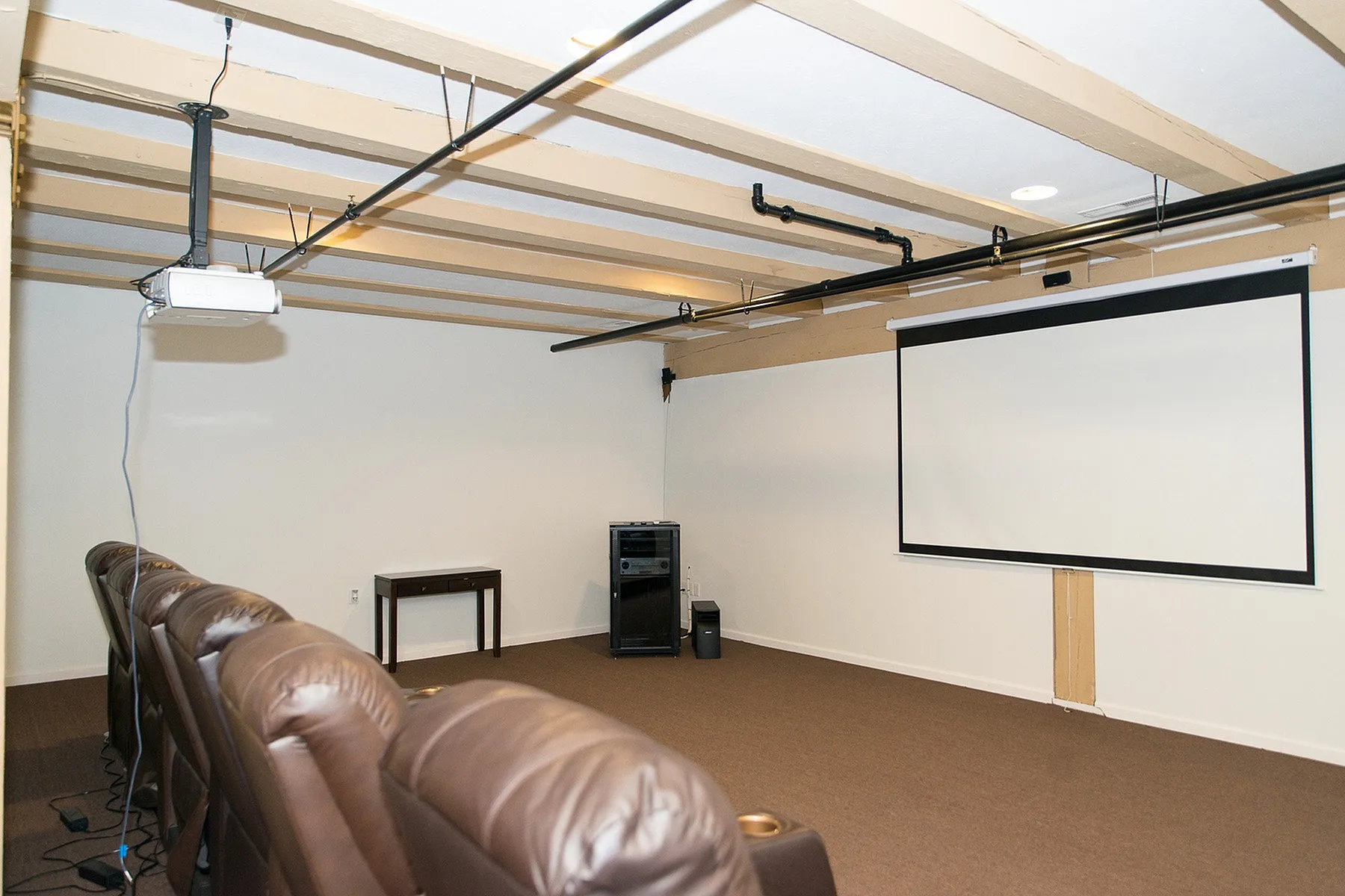 Modern home theater with plush seating, ceiling projector, and a large screen in a cozy room.
