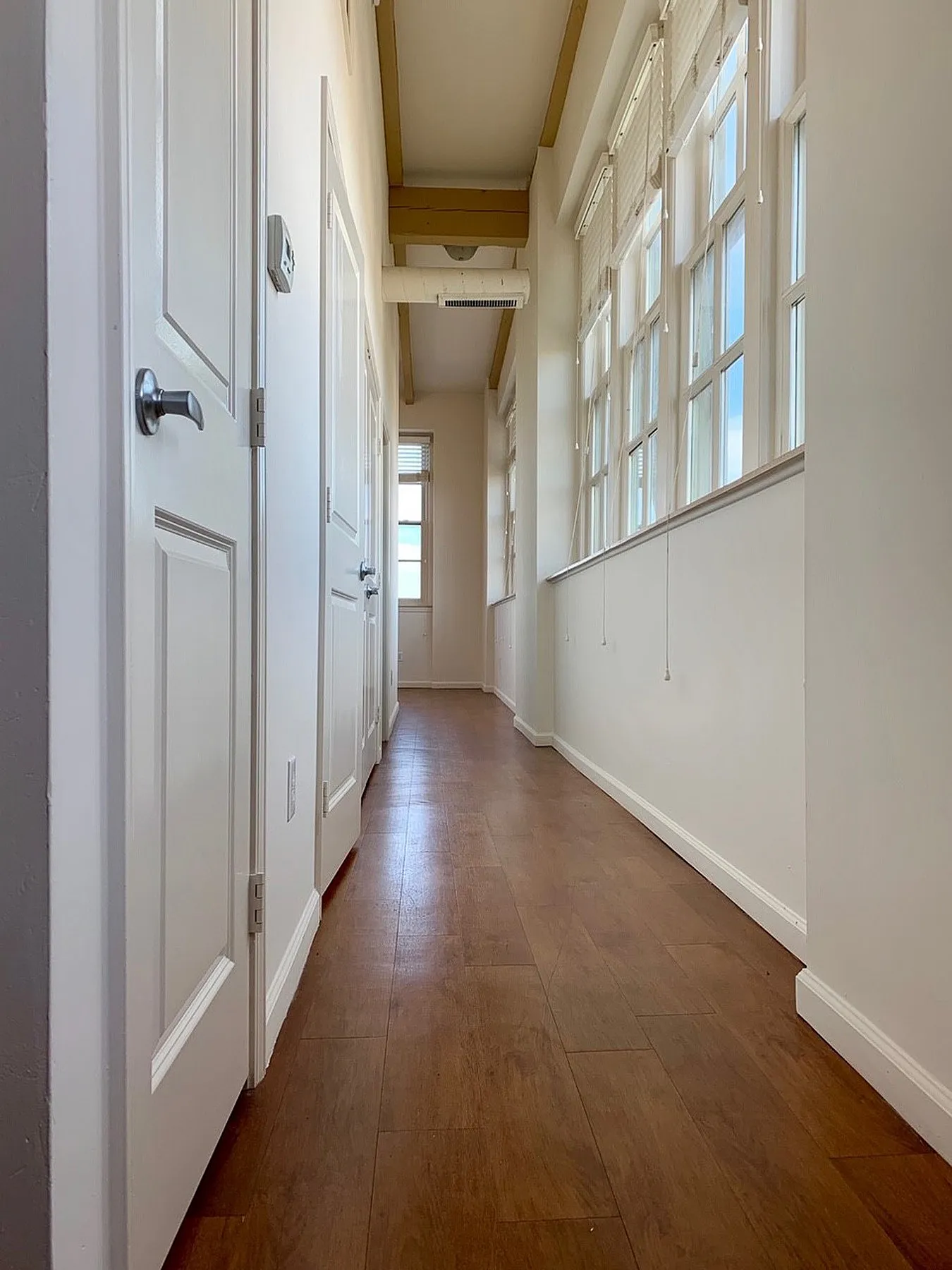 Inviting hallway with elegant wooden flooring and large windows allowing natural light.