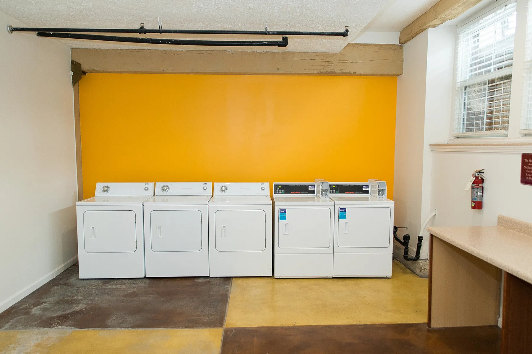 Bright and efficient laundry room with multiple modern dryers and vibrant orange accent wall, creating a welcoming atmosphere.