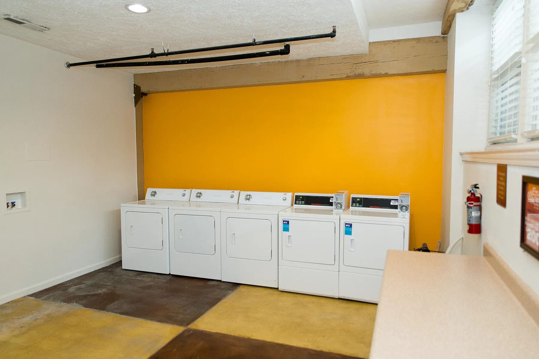 Bright laundry room featuring multiple modern washing machines against a vibrant yellow accent wall, offering convenience and style.