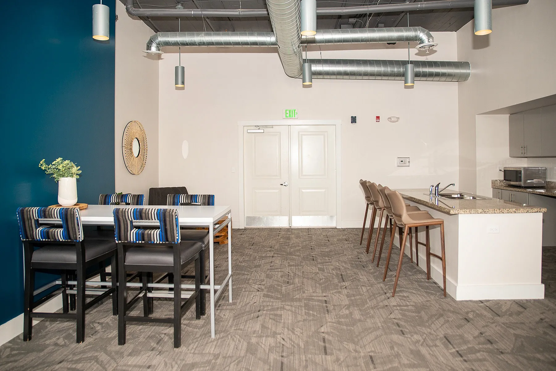 Modern communal space featuring a sleek dining area with stylish seating, vibrant blue accent wall, and an inviting kitchen island with bar stools.