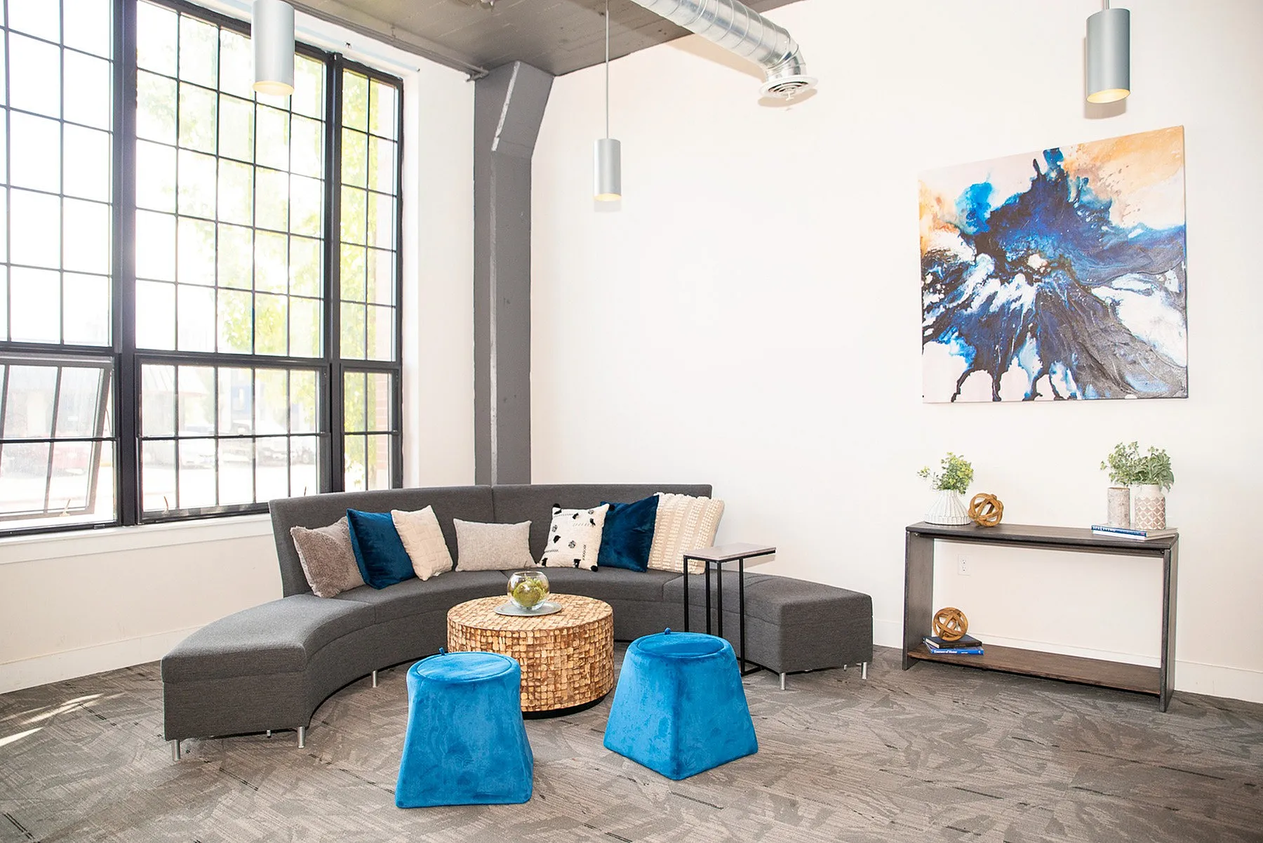 Bright and modern living area featuring a curved gray sofa, vibrant blue stools, and abstract wall art.