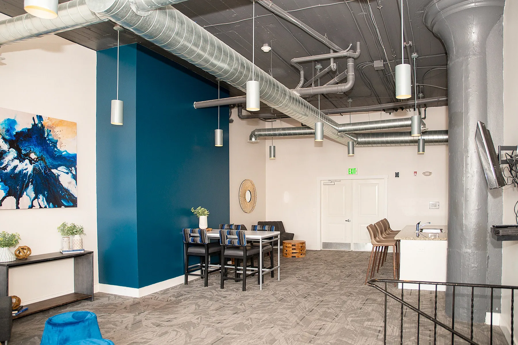 Chic industrial loft lounge with modern exposed ductwork, bold blue accent wall, and plush seating areas.