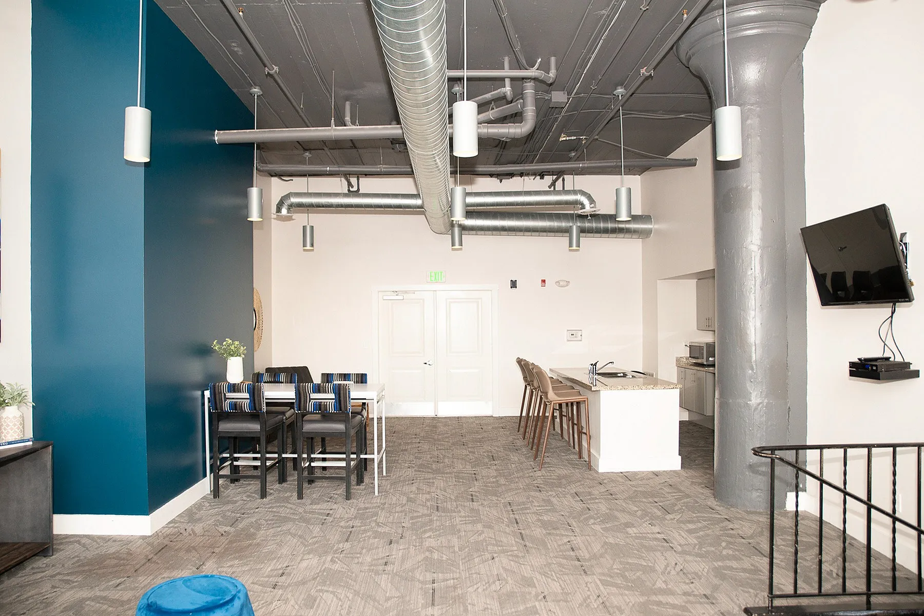 Modern open-concept kitchen and dining area with high ceilings, exposed ductwork, a stylish blue accent wall, and sleek fixtures.