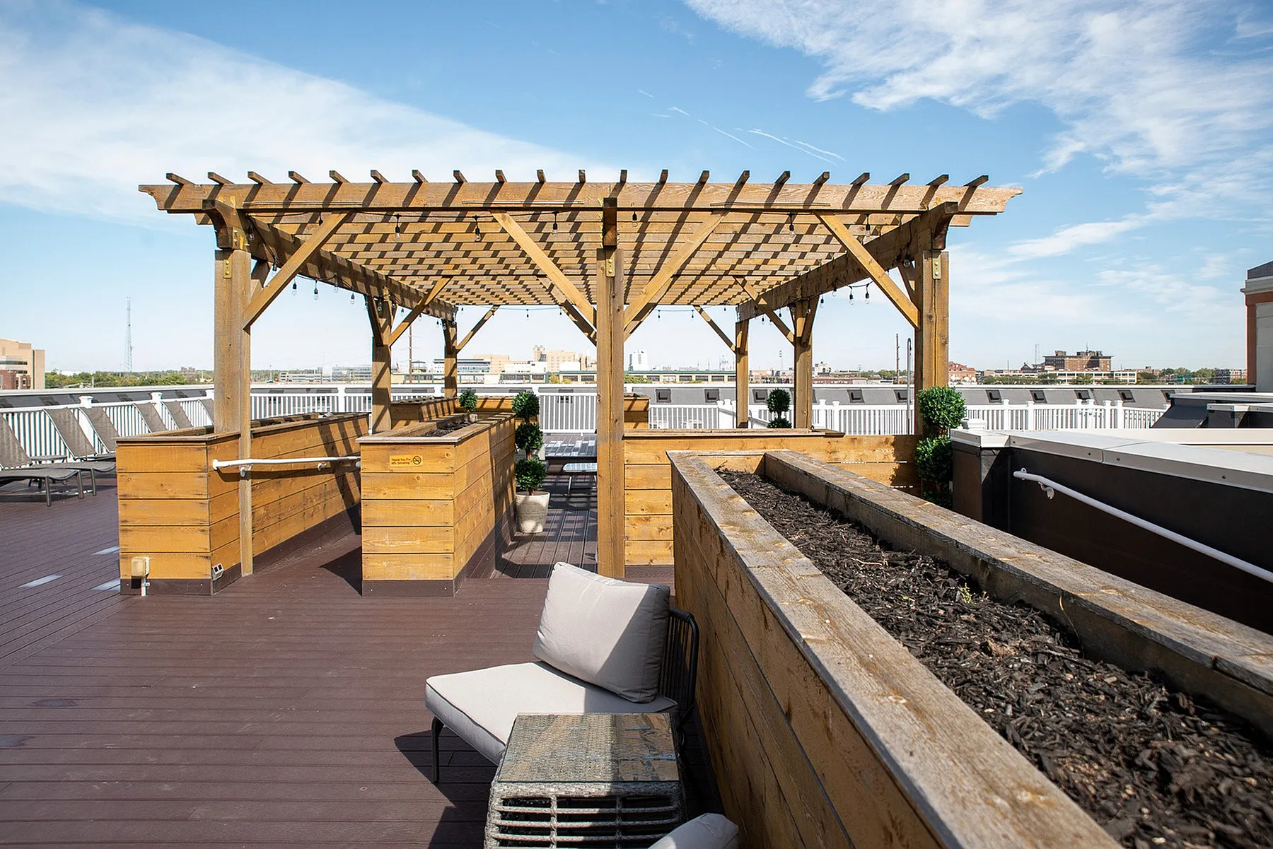 Chic rooftop terrace featuring a wooden pergola, modern lounge seating, and planters offering stunning sky views.