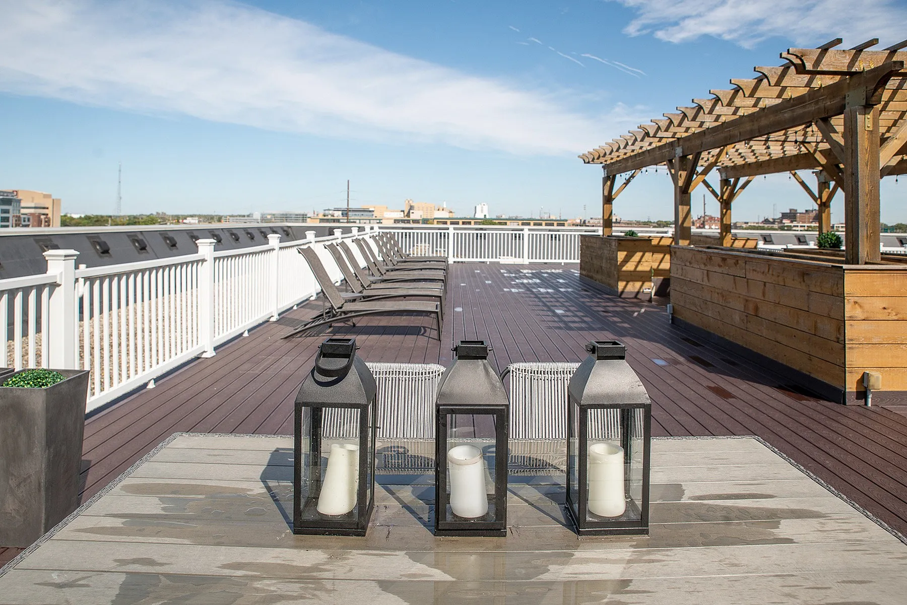 Chic rooftop patio featuring elegant lounge chairs, stylish lanterns, and a wooden pergola under a sunny sky.