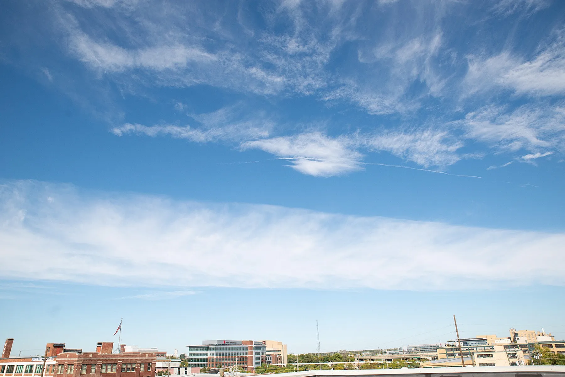 Bright urban skyline under a clear blue sky with artistic clouds, showcasing modern buildings and a vibrant cityscape.