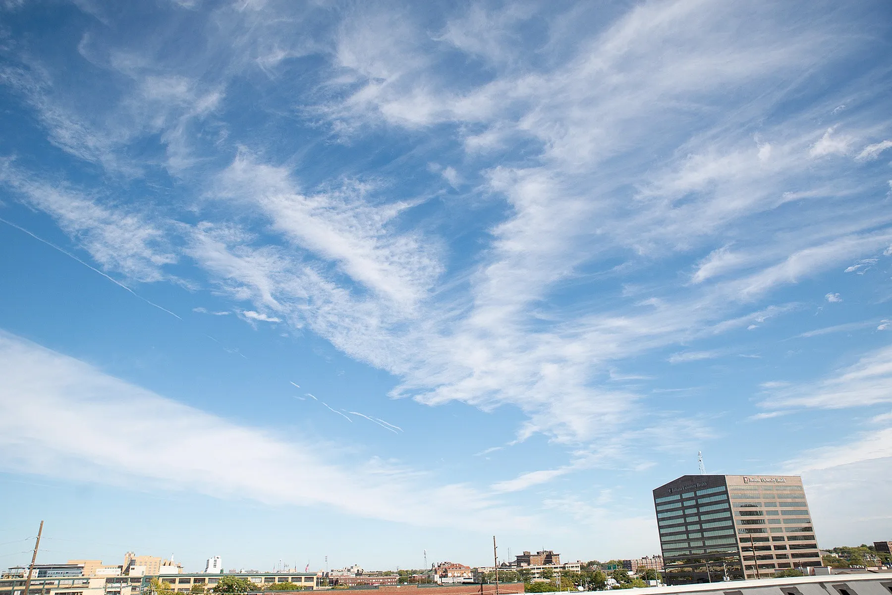 Vibrant cityscape under a bright blue sky with wispy clouds and a towering office building, offering expansive views.