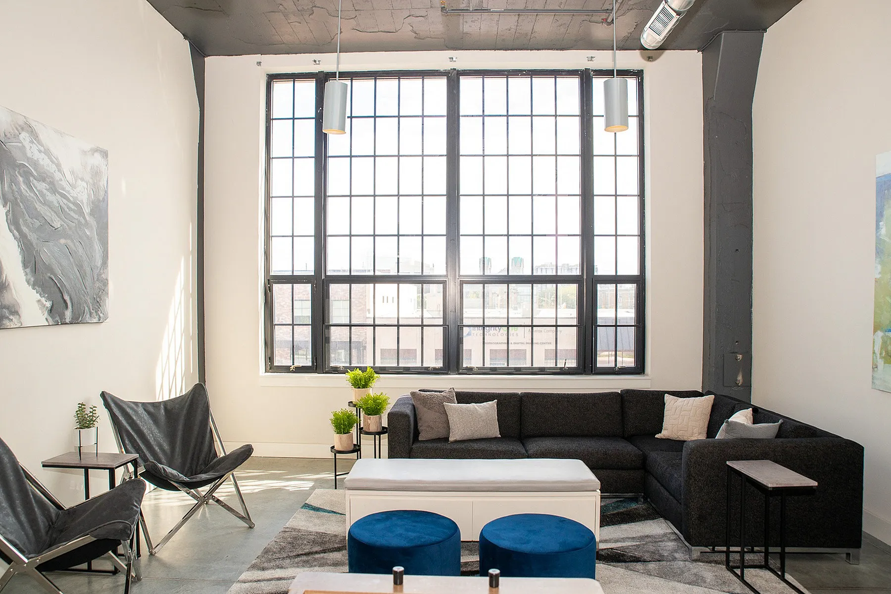 Bright and contemporary living room with stylish black furniture, large industrial windows, and modern decor.