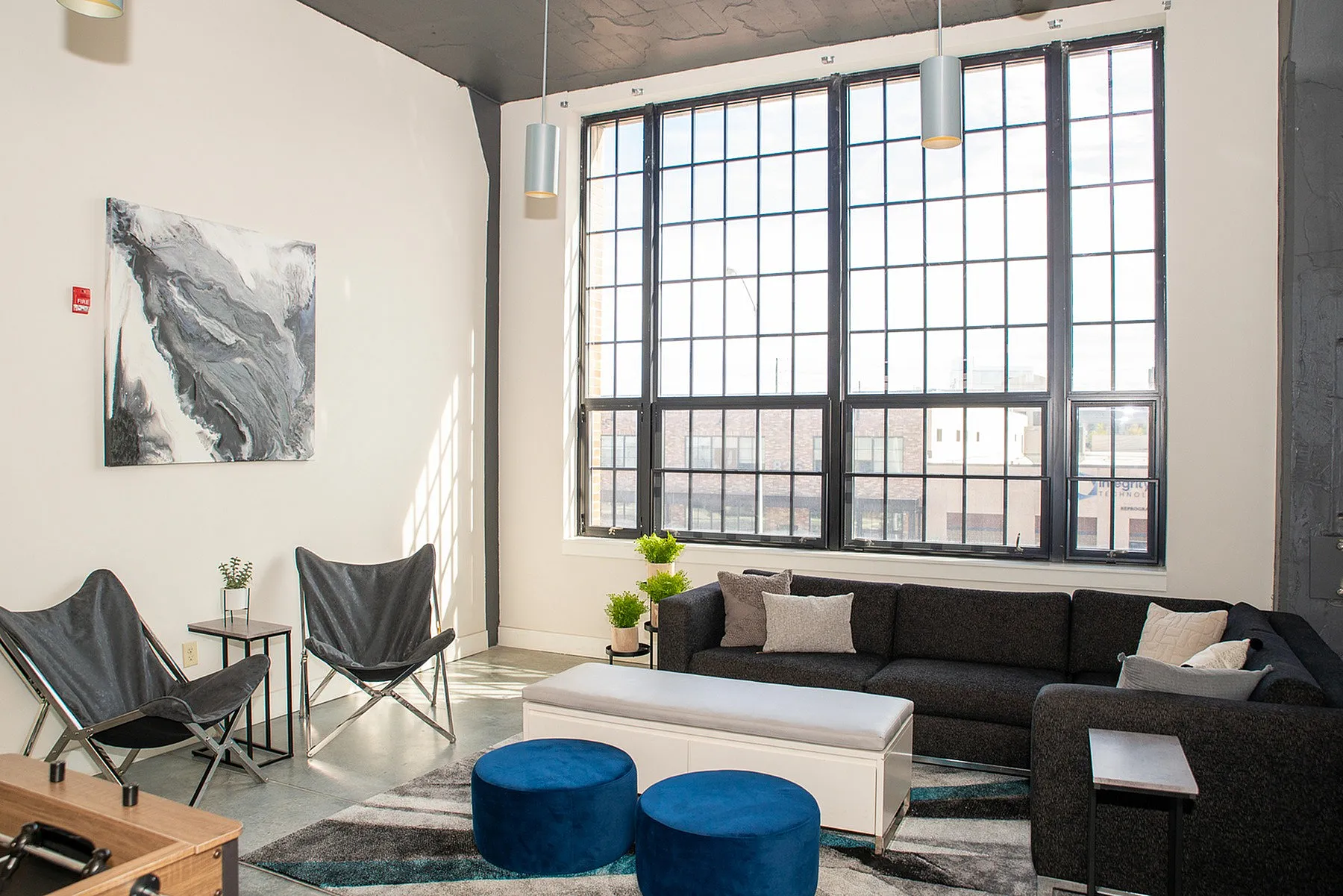 Bright and modern living room with a large window, cozy dark sofa, chic decor, and stylish seating accents.