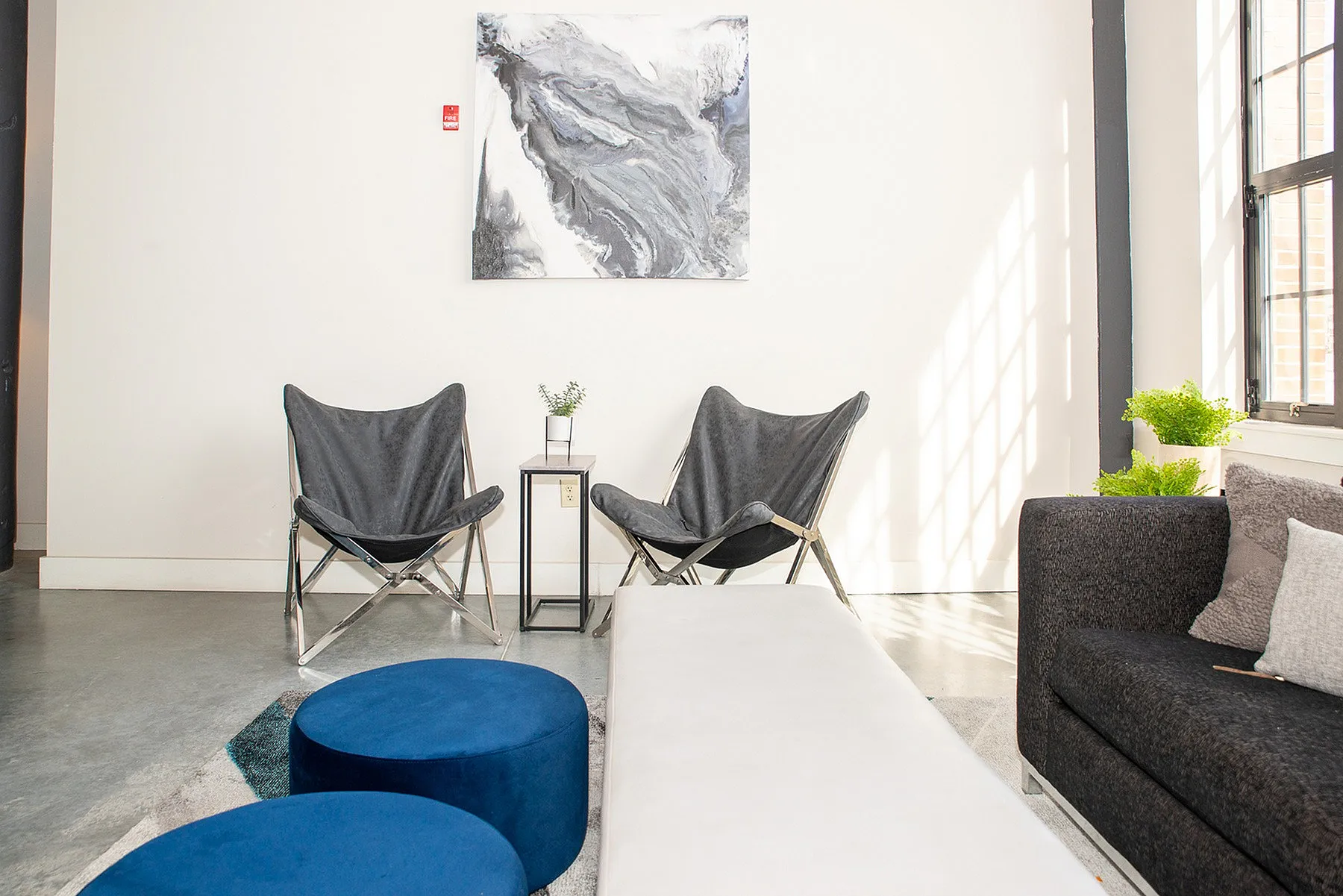 Modern living space with chic gray chairs, abstract wall art, and large windows providing ample natural light.