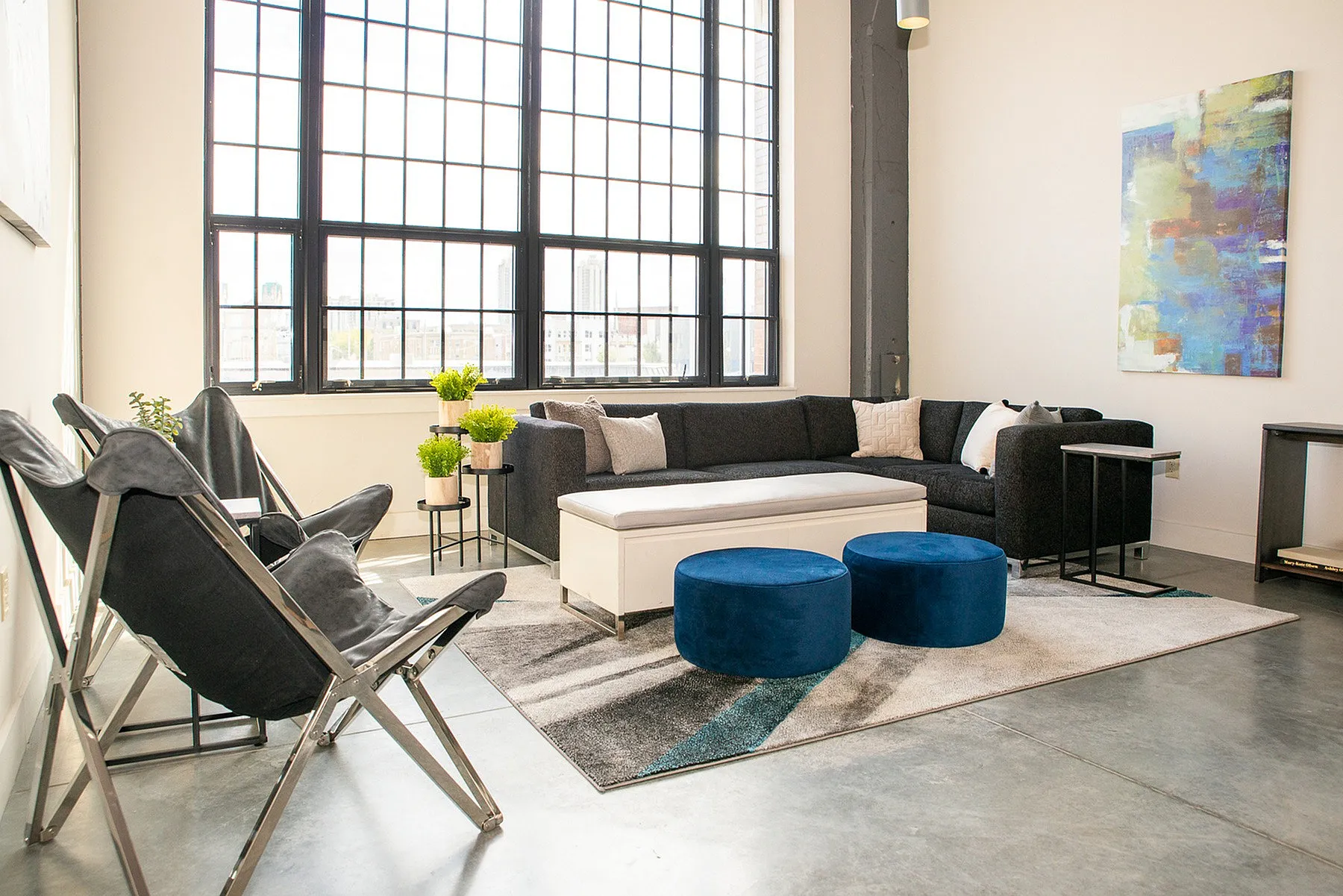 Bright and modern living room with expansive windows, cozy dark sectional, and stylish decor in an urban setting.