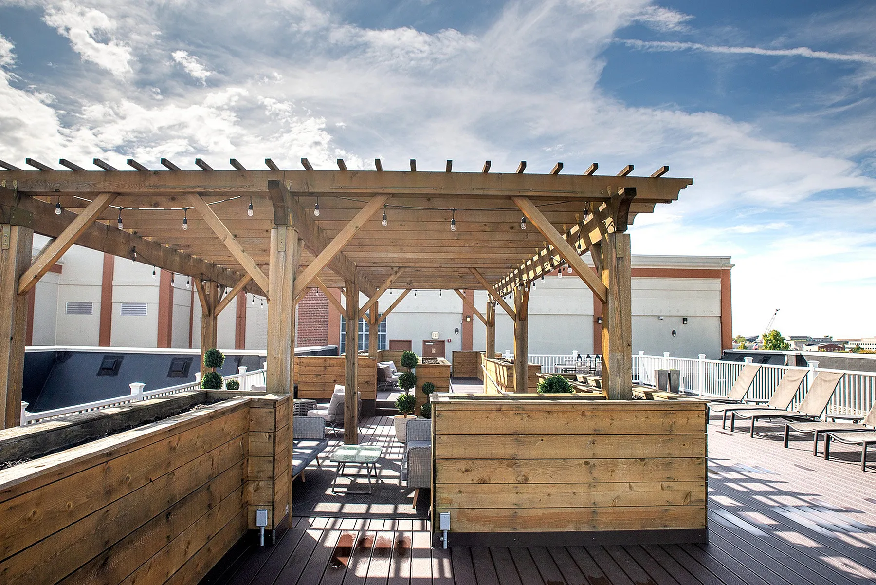 Chic rooftop terrace with elegant wooden pergolas, stylish seating, and panoramic city views under a clear blue sky.