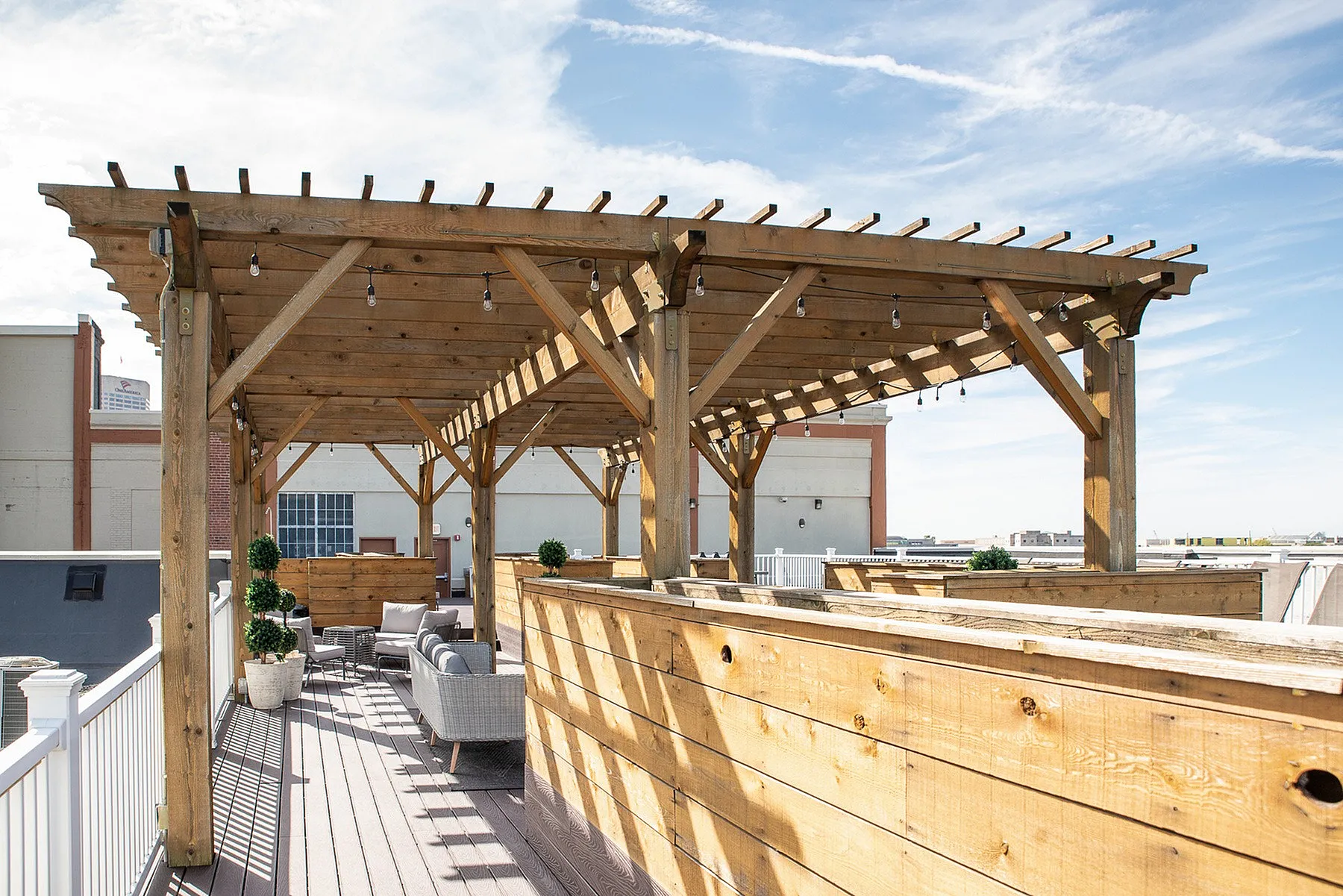 Charming rooftop terrace featuring a wooden pergola, cozy outdoor seating, and vibrant potted plants under a clear blue sky.