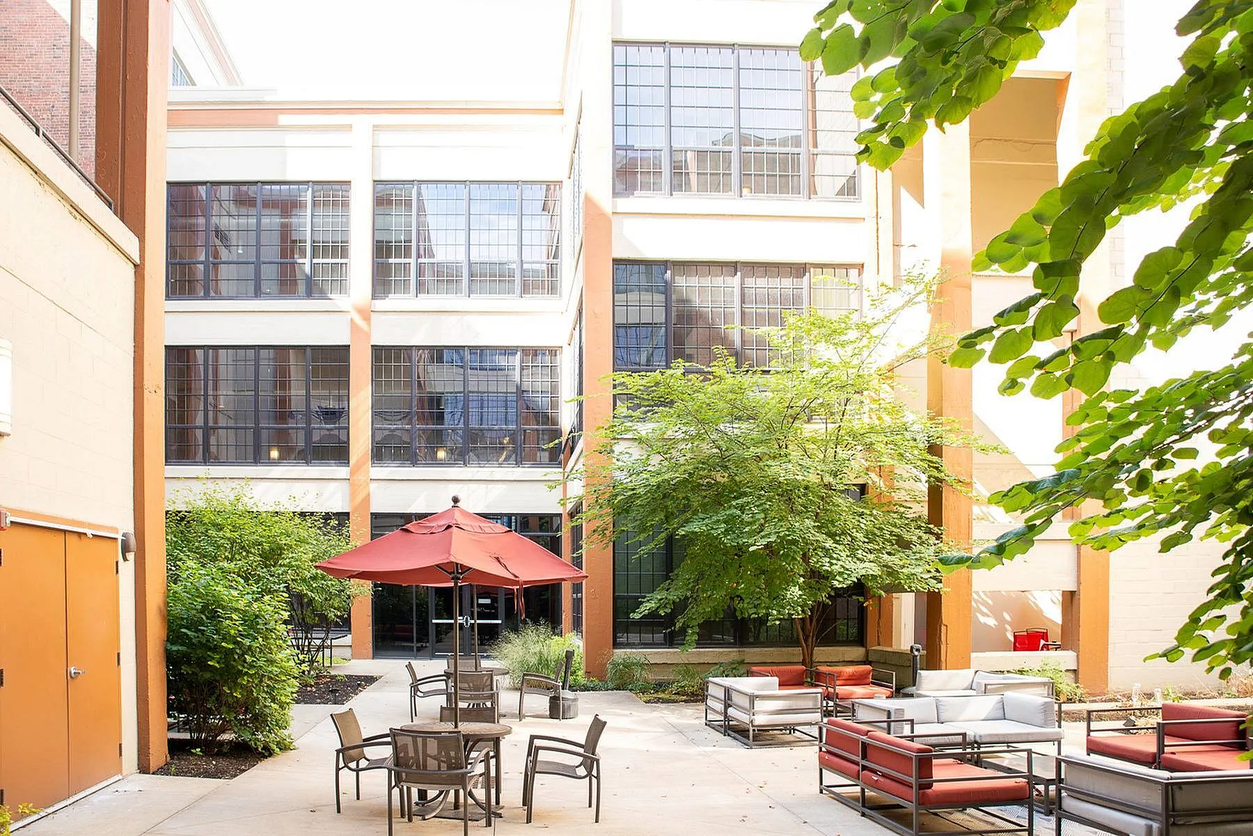 Charming urban courtyard with cozy seating, umbrella-shaded tables, and lush greenery, perfect for relaxation and social gatherings.