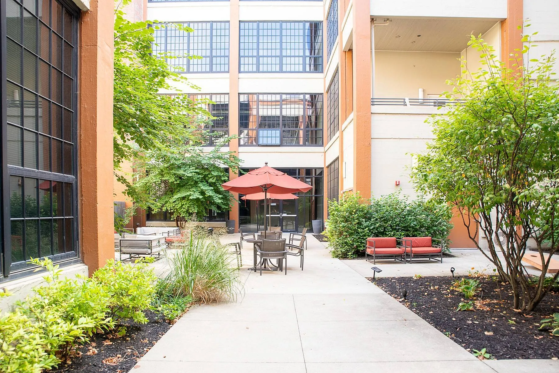 Charming courtyard view with lush greenery, stylish outdoor seating, and vibrant umbrellas, perfect for relaxation and gatherings.