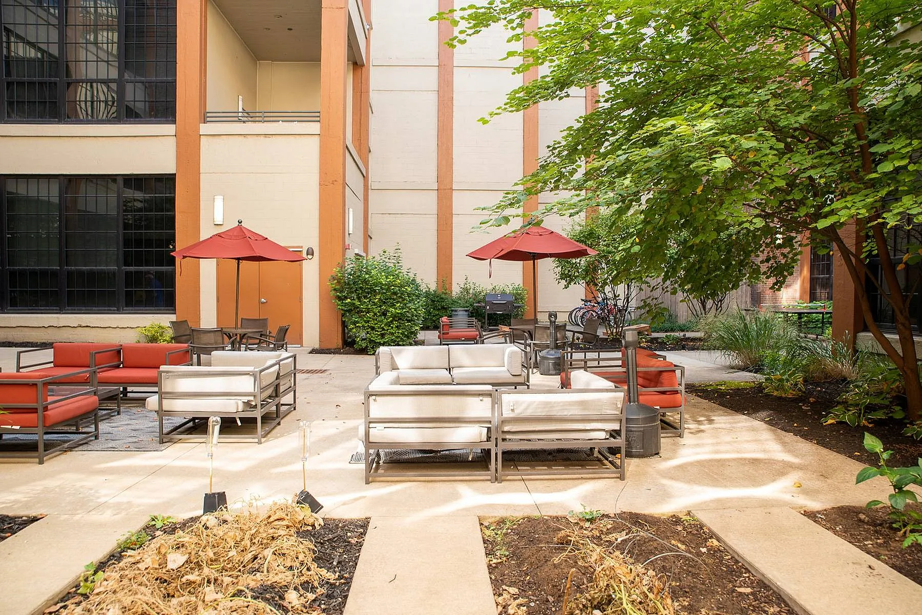 Charming outdoor courtyard with modern seating, vibrant red umbrellas, and lush greenery offering a serene retreat.