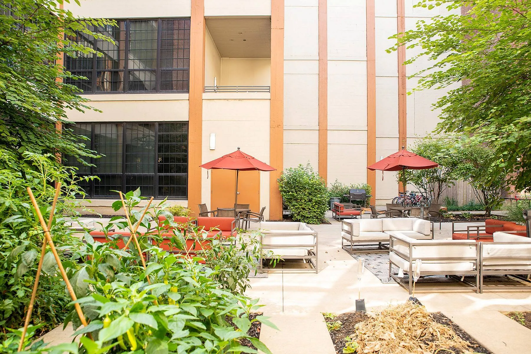 Charming outdoor courtyard featuring lush greenery, modern seating, and vibrant red umbrellas for a relaxing urban retreat.