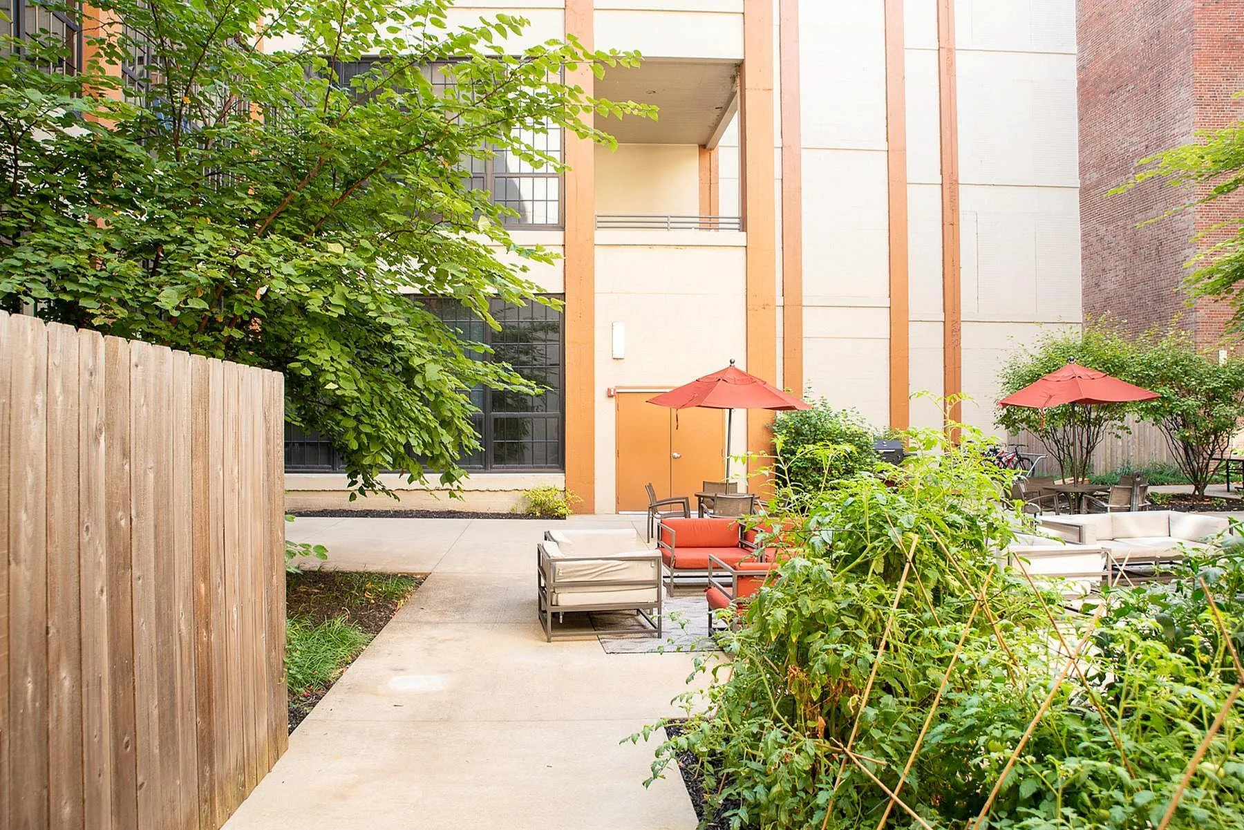 Charming outdoor courtyard with lush greenery, cozy seating, and vibrant red umbrellas providing a perfect relaxation spot.