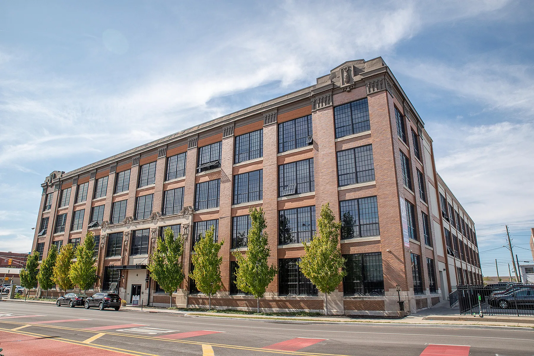 Charming brick building with large grids of windows and modern design, flanked by lush green trees, promising a vibrant urban living experience.