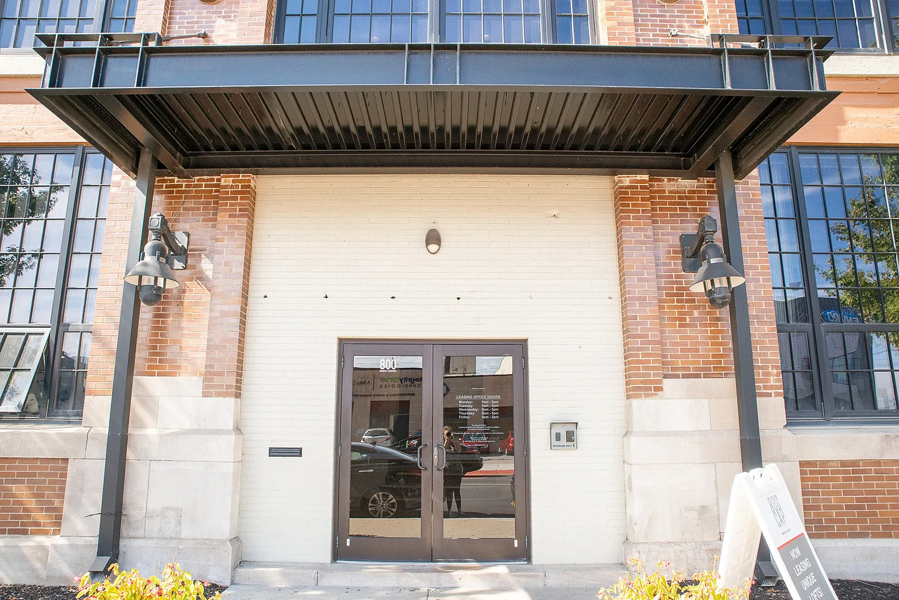 Charming industrial-style entrance with large windows, featuring rustic brickwork and modern lighting, inviting residents to a trendy urban apartment building.